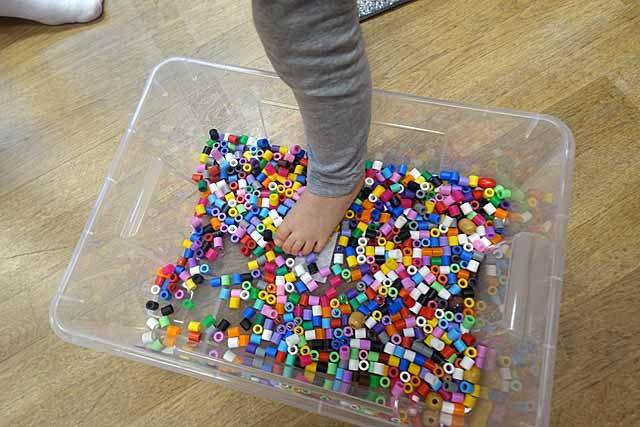 Kind steht mit einem Fuß in Kiste mit Legosteinen, Thema experimentieren "mit allen Sinnen"