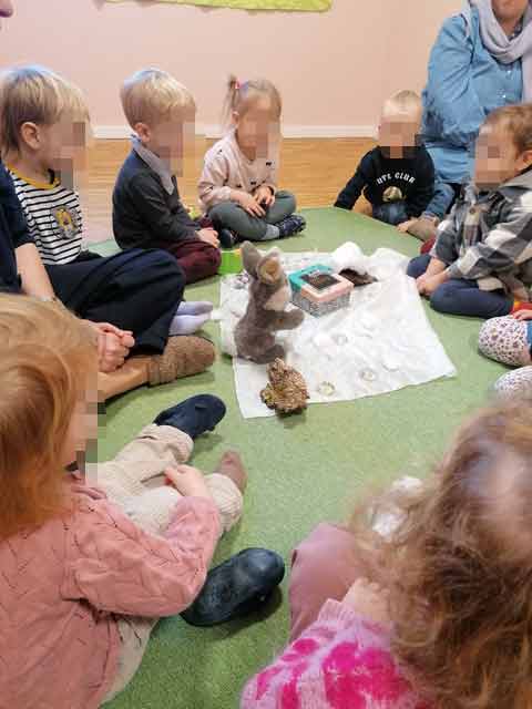 Mehrere Kinder sitzen am Boden und hören und spielen die Geschichte Hase in der Schneelandschaft