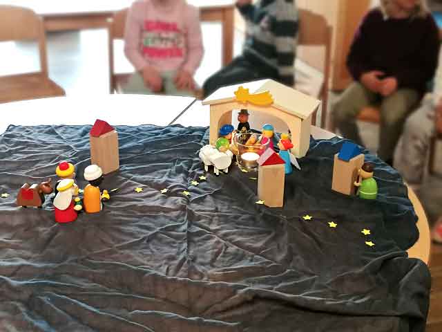 Kinder sitzen um einen Tisch, lernen die Weihnachtsgeschichte kennen