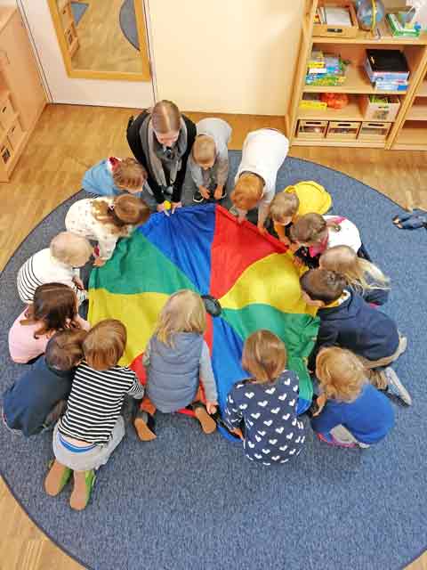 Kinder sitzen um ein buntes Tuch zum Start der Farbenwoche