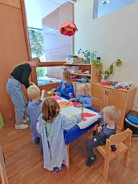 KInder sitzen am Tisch und malen mit Wasserfarben