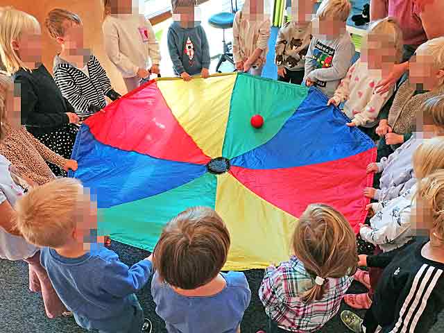 Kinder stehen im Kreis und lassen den Ball im Tuch rollen
