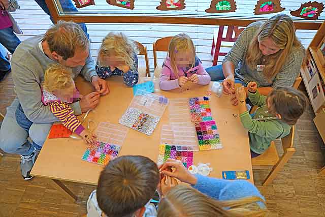 Kinder sitzen um einen Tisch um Perlarmbänder zu fädeln
