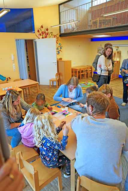 Kinder sitzen mit Eltern um einen Tisch um Perlarmbänder zu fädeln