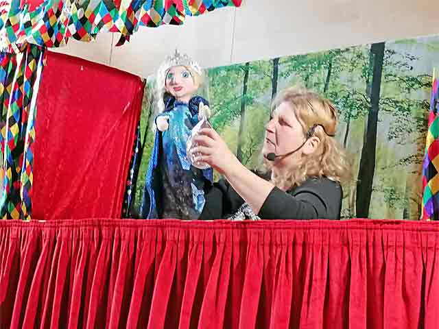 Eine Puppenspielerin steht mit einer Handpuppe hinter der Bühne