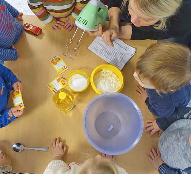 Zutaten für selbst hergestellte Knete stehen auf dem Tisch und Kinder sitzen dabei