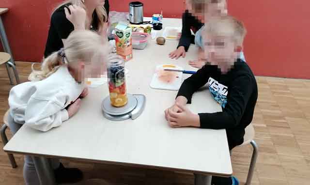 Kinder sitzen am Tisch und stellen ein Smoothie her.